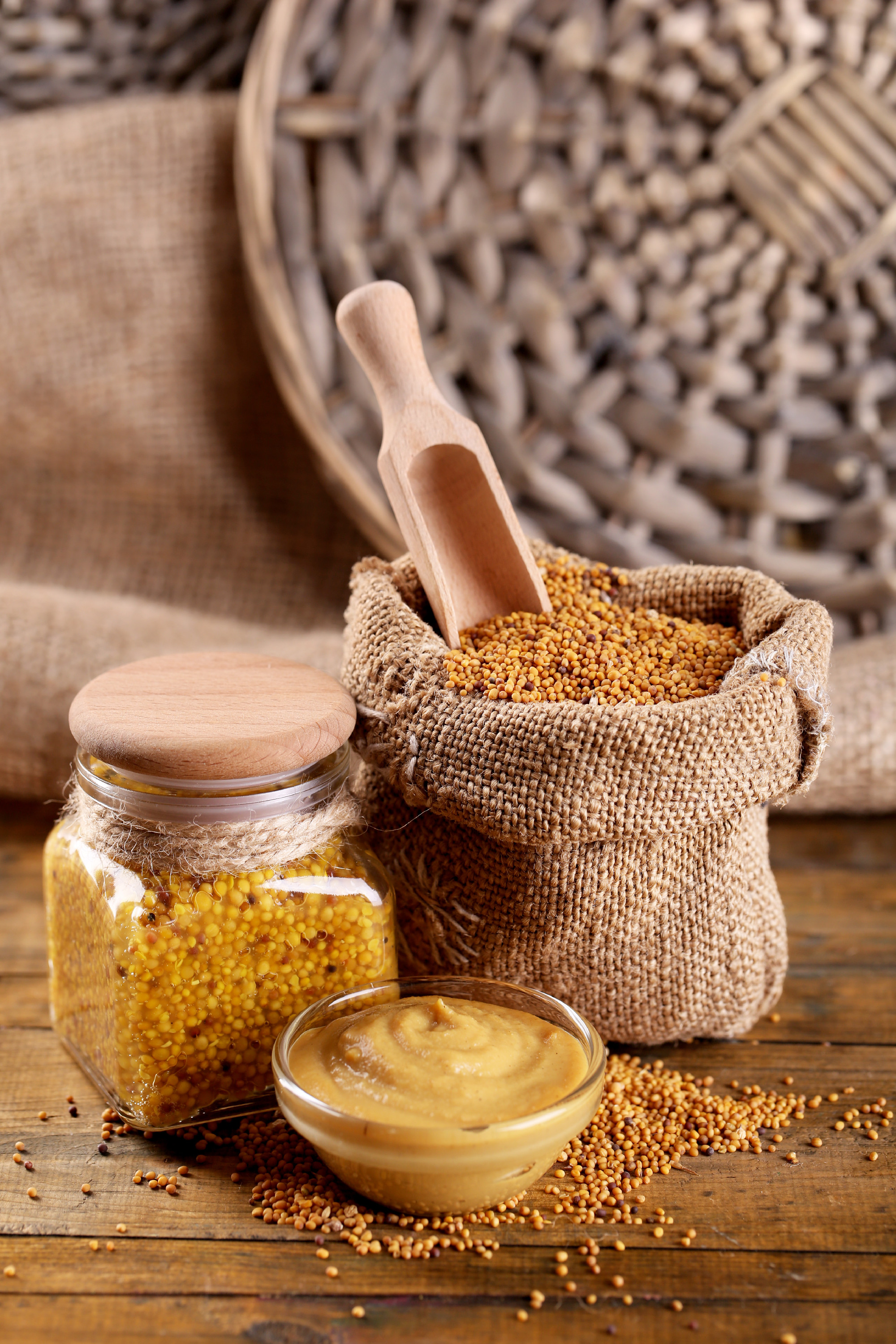 Mustard seeds in bag and sauce in sauce-boat on wooden background