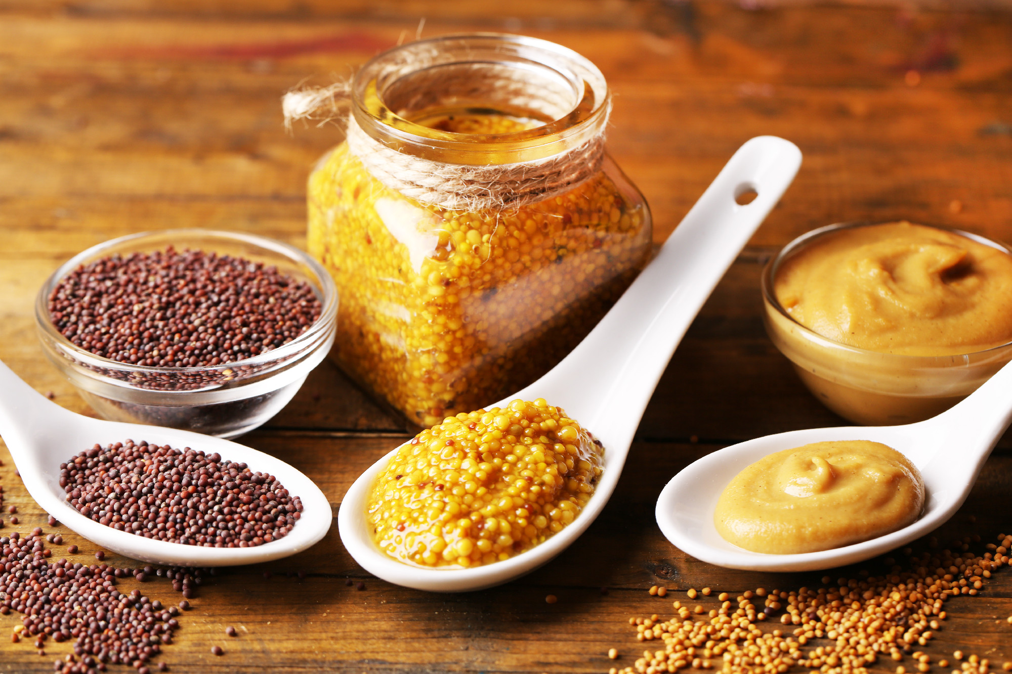 Mustard seeds, powder and sauce in spoons, bowls and glass jar on wooden background