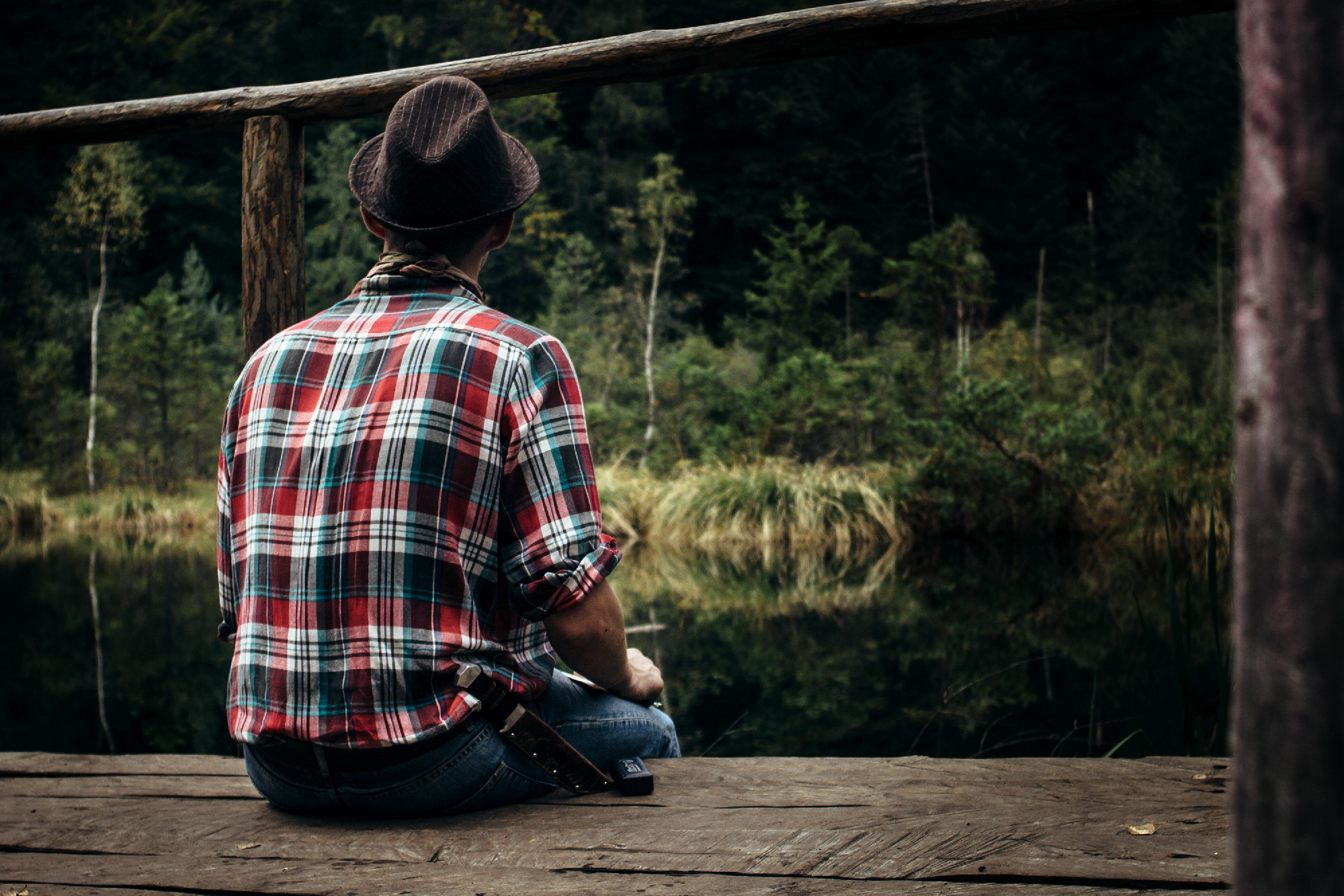 stylish hipster traveler sitting at sunny forest and lake in the