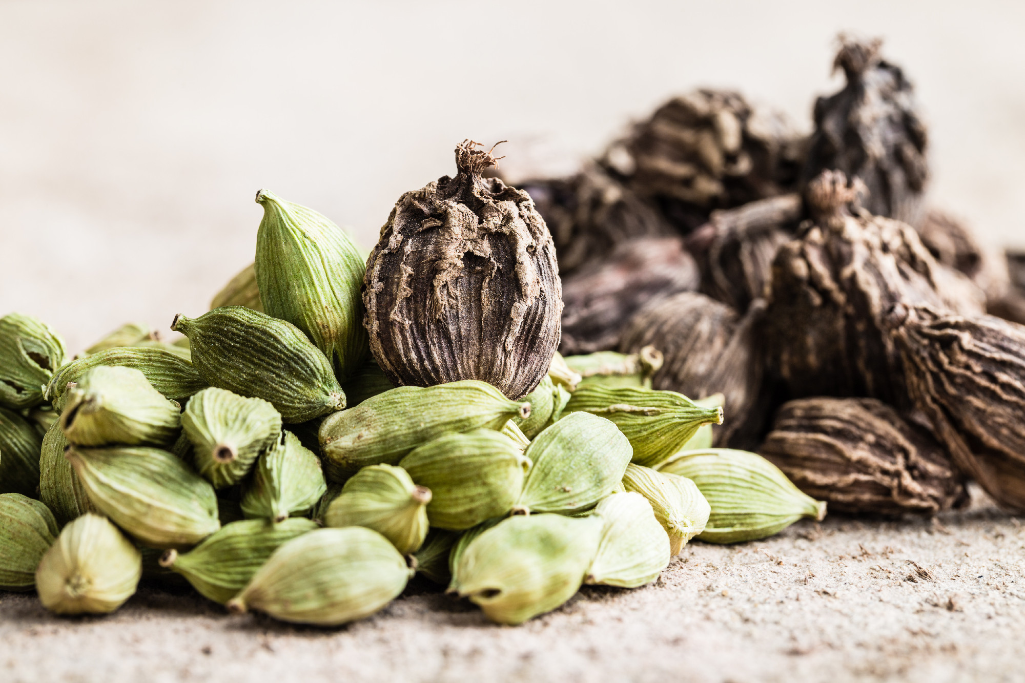 Black and green cardamom whole seeds on wooden background.