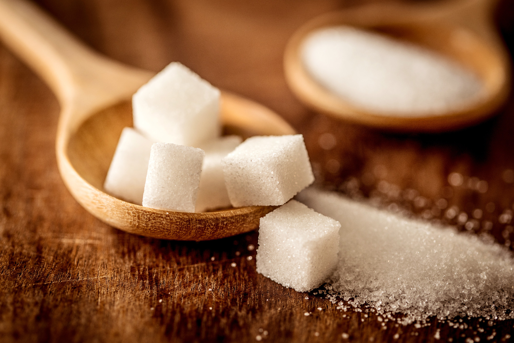 Close up white sugar cubes and cane in wooden spoon on the table