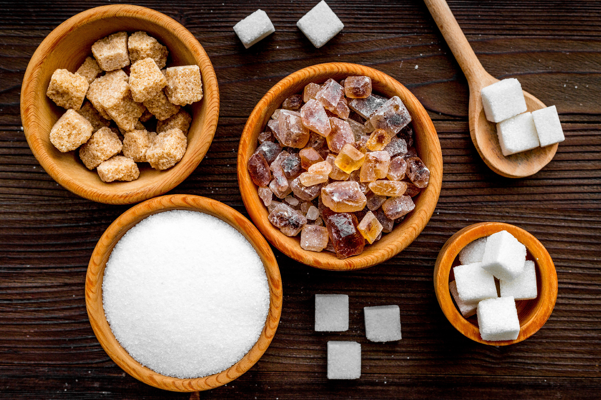 Sugar background on dark wooden table. Bowls with different kinds of sugar. Top view