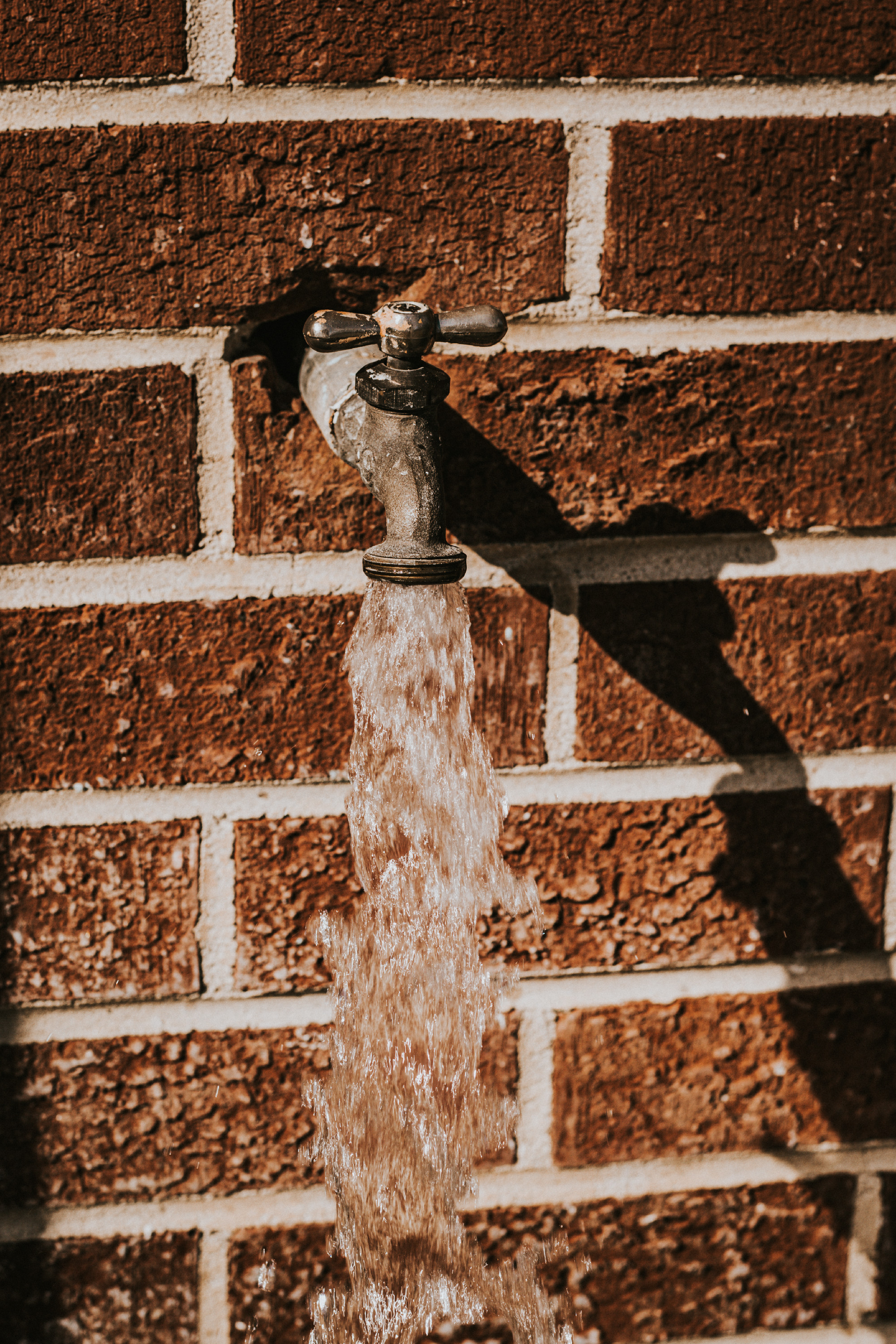 Closeup of water flow from a metal faucet on a brick wall
