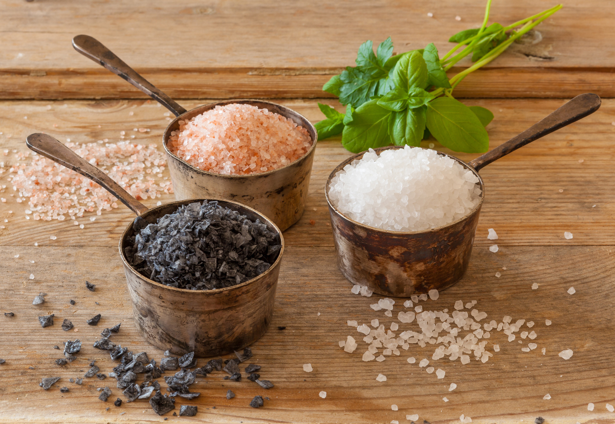 Three different types of salt in silver containers on a worn out
