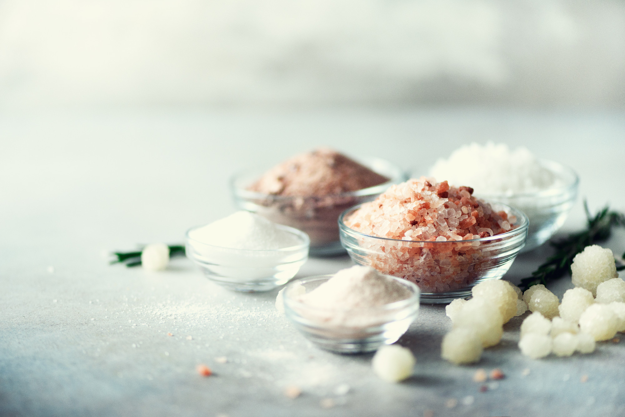 Mix of different salt types on grey concrete background. Sea salts, black and pink Himalayan salt crystals, powder, rosemary. Salt crystal balls from Dead sea. Copy space