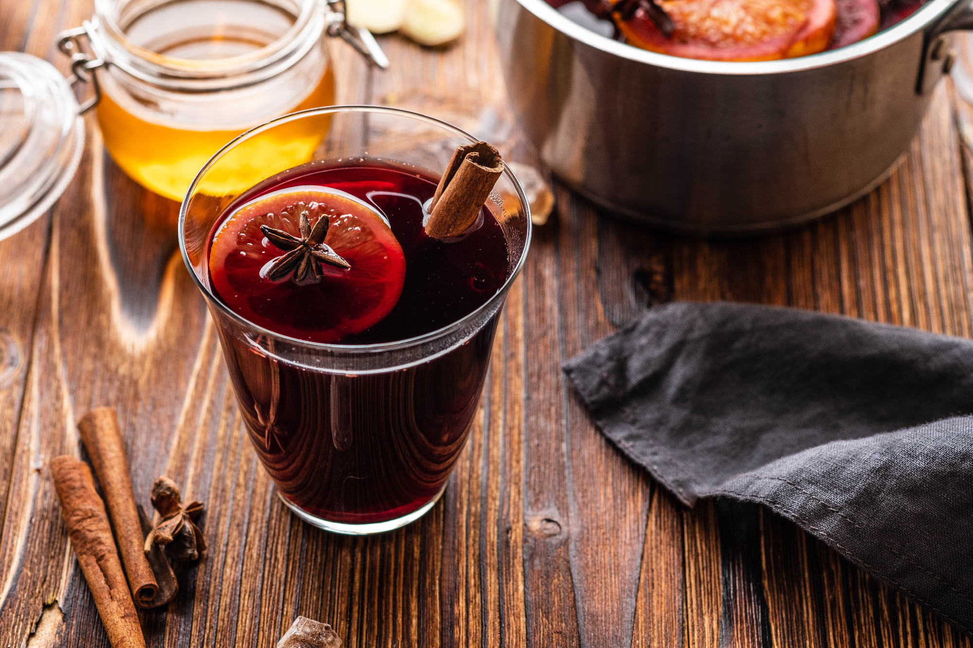 Hot mulled wine with spices, citrus and honey on woodern background. Copy space.