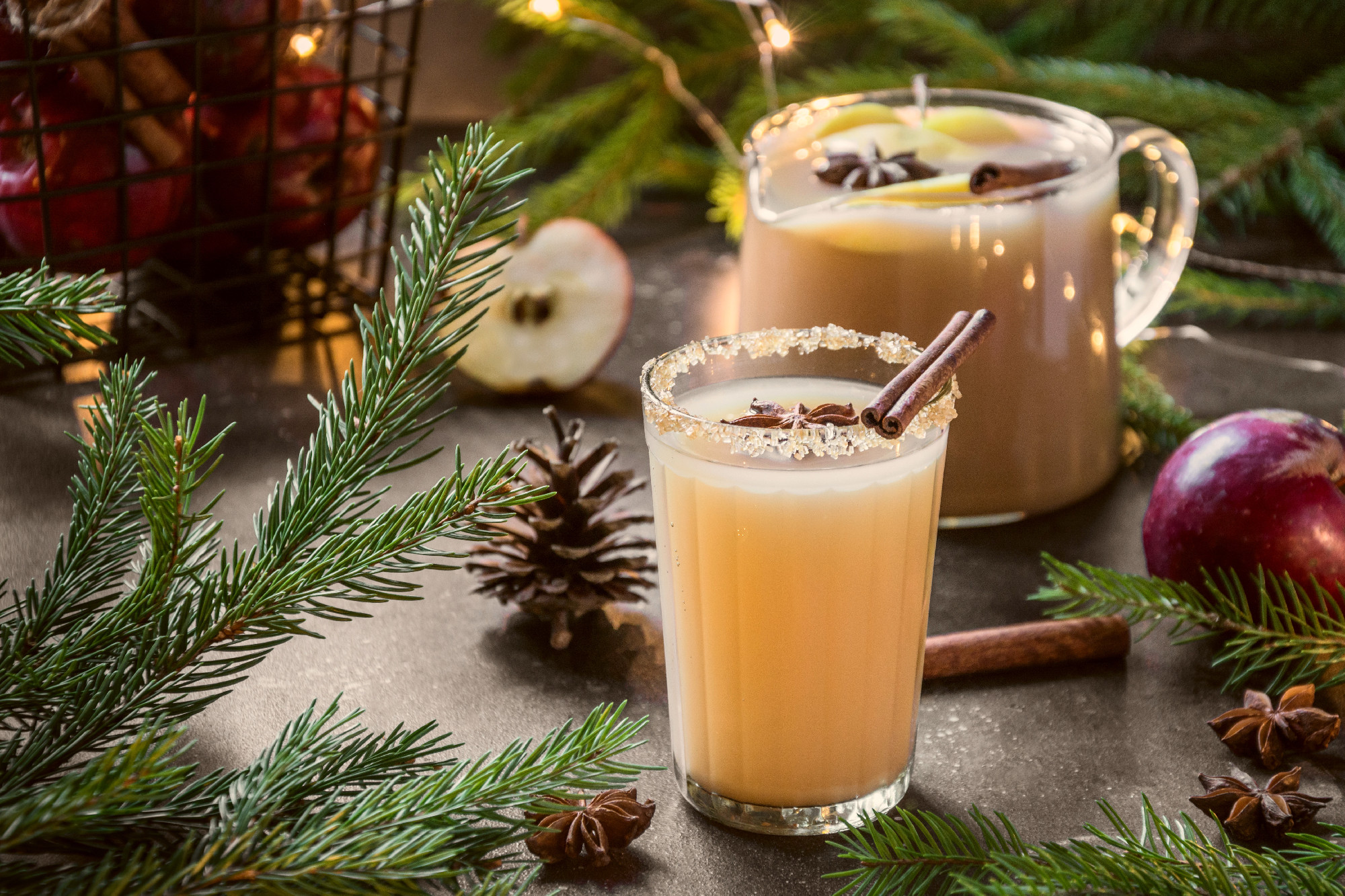 Apple cider cocktail with cardamom and star anise on black table with fir tree branches.