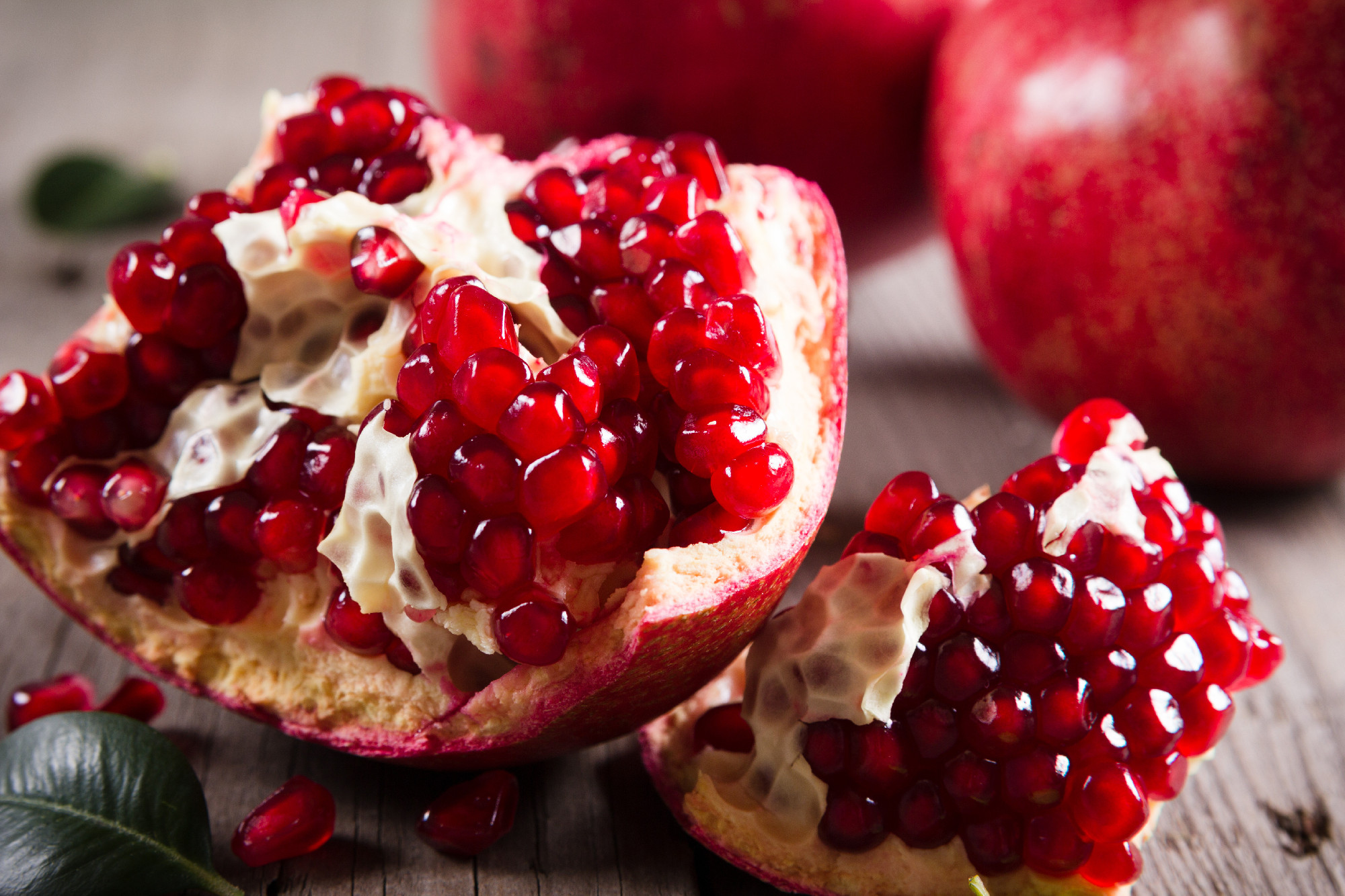 Whole and broken red ripe juicy pomegranates on rustic wooden unpainted table