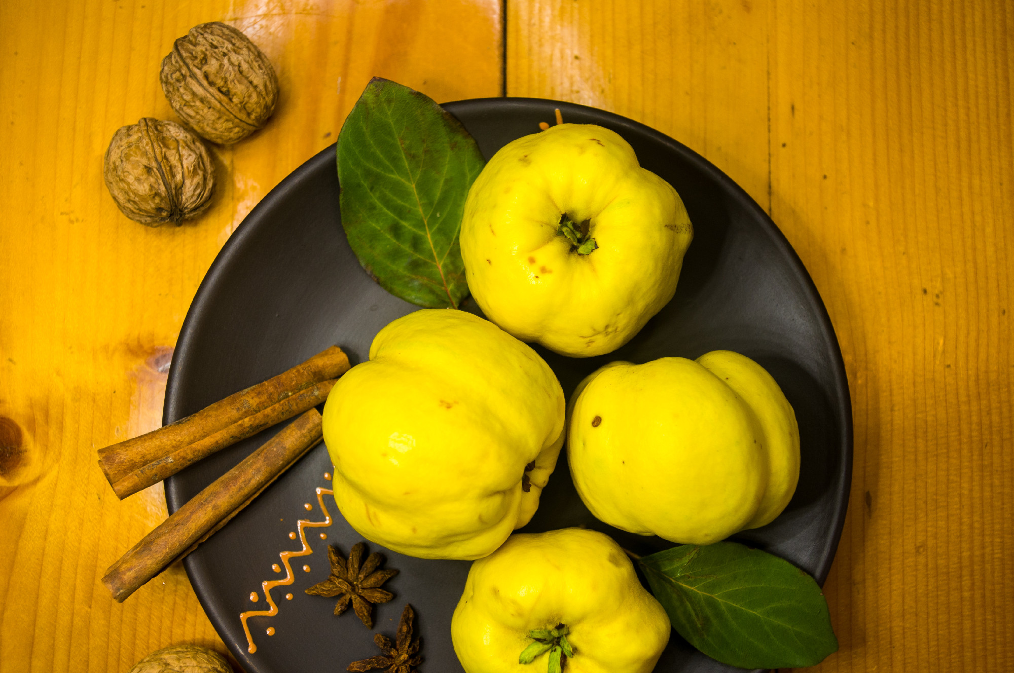 large yellow quince fruits on a ceramic plate, with anise, cinnamon, and walnuts
