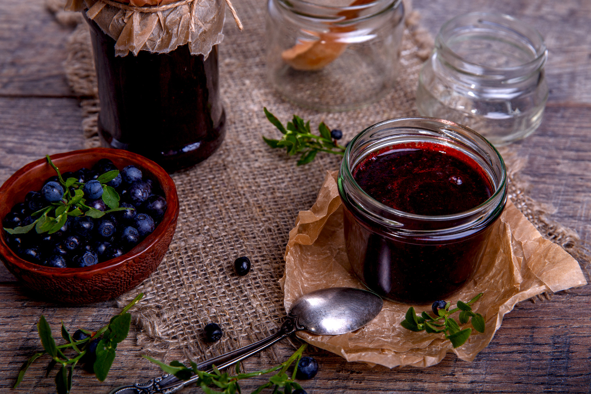 Blueberry jam in jar with berries and leaves over rustic wooden