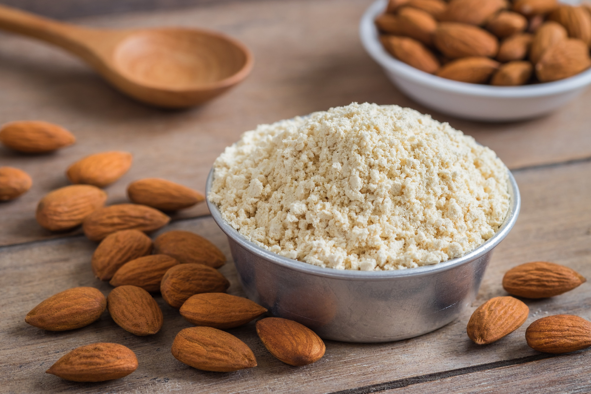 Almond flour in bowl and almonds on wooden table