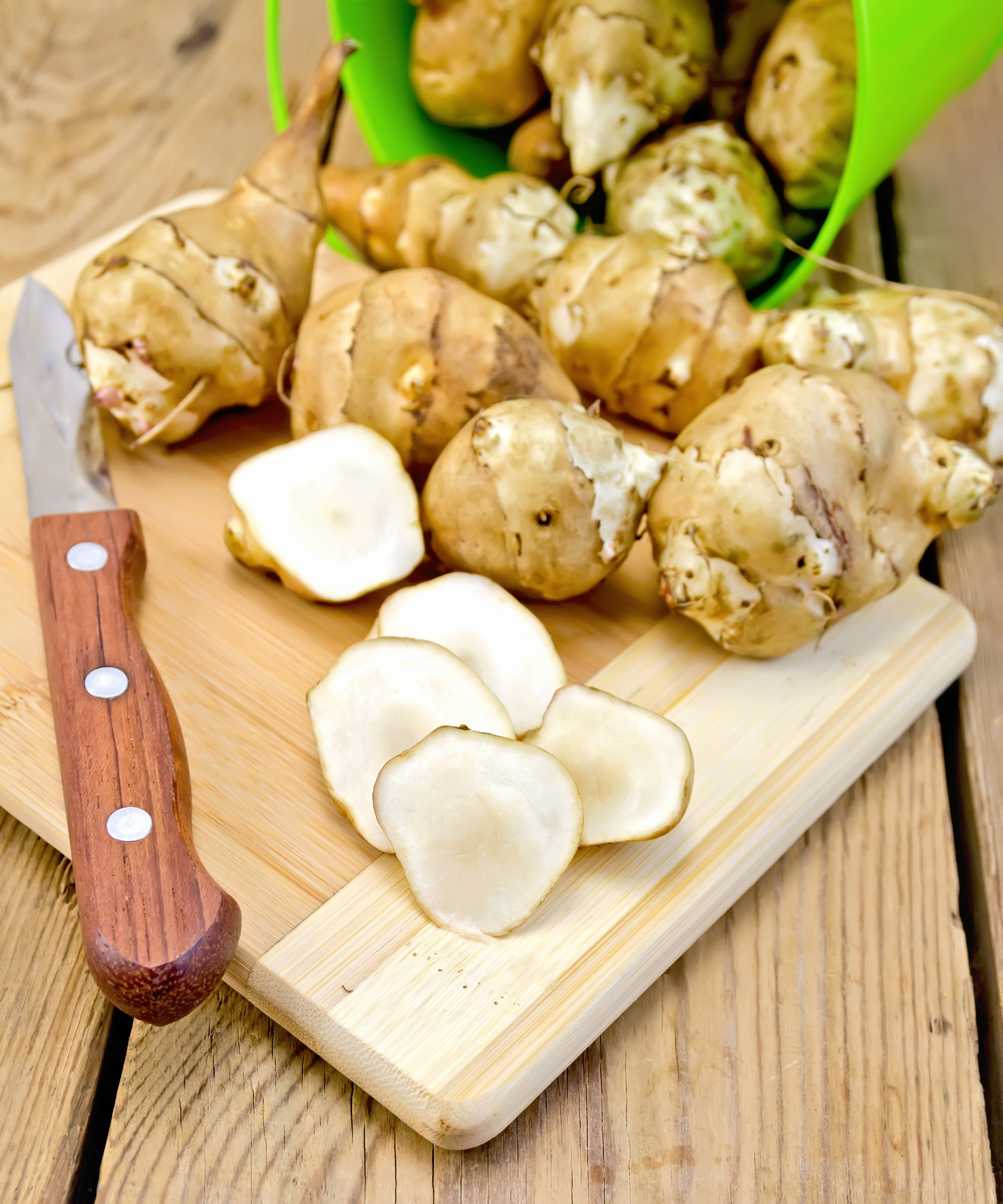 Jerusalem artichokes cut with knife and green bucket on board
