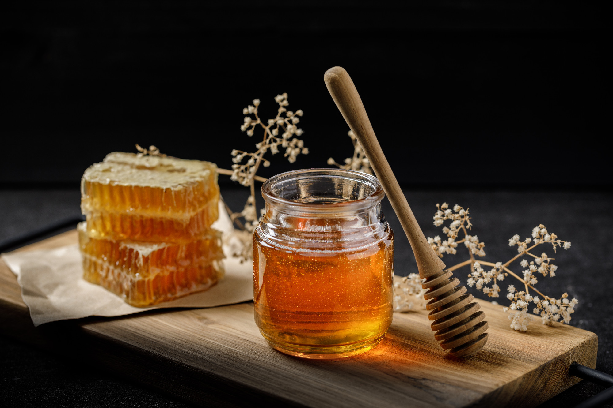 Honeycomb with honey dipper and dry flower on black background,