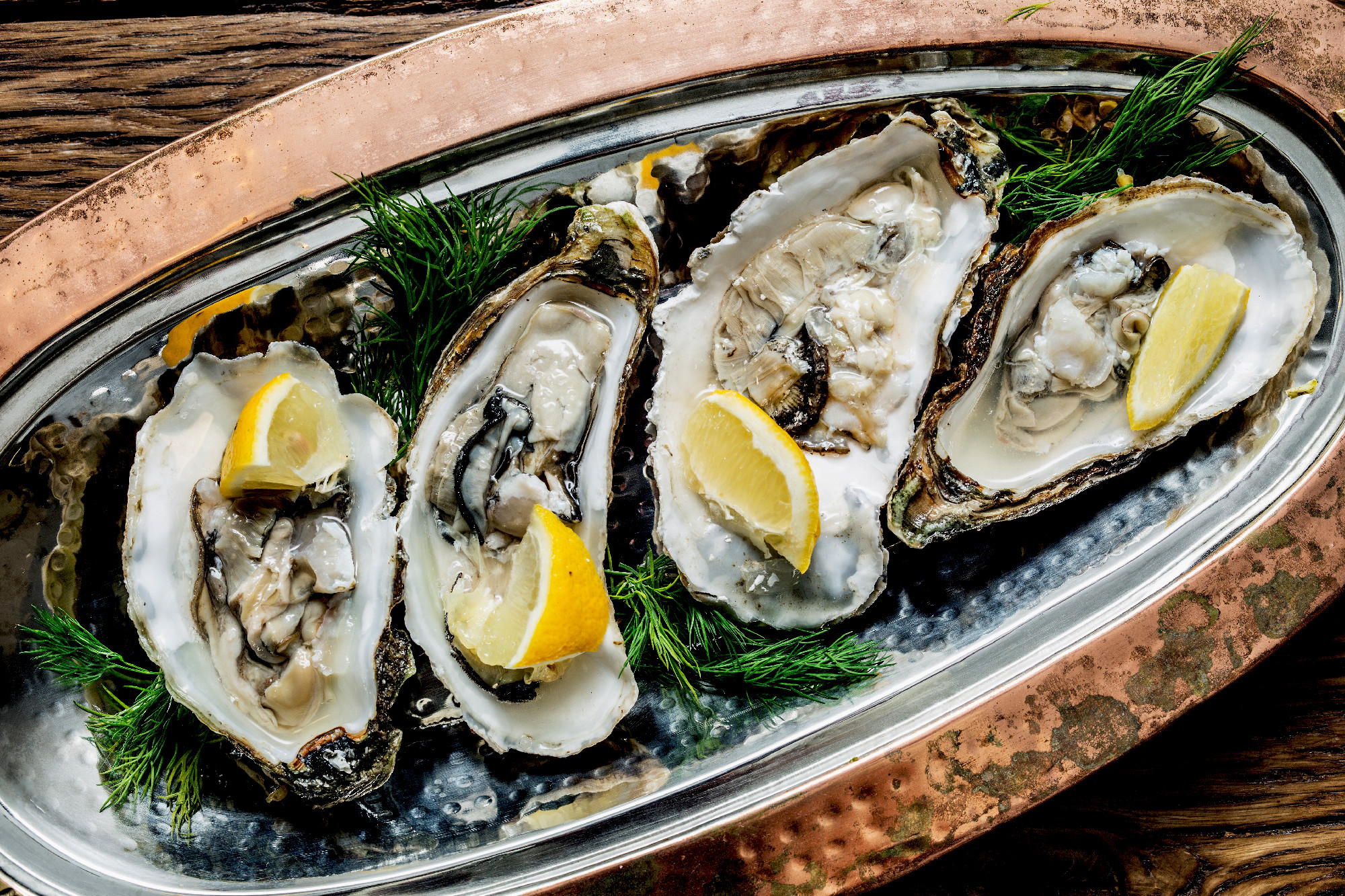 Opened oysters with piece of lemon on the cooper tray.