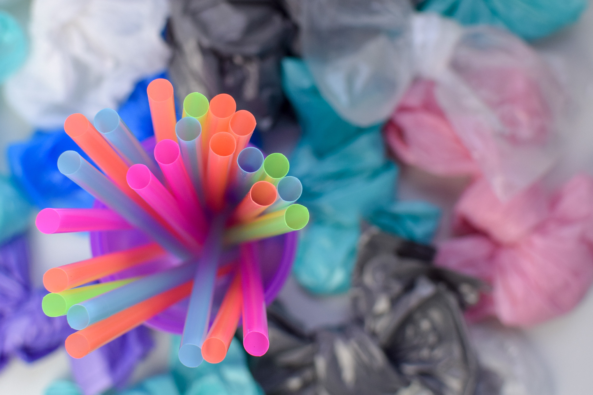 Bright multicolored plastic tubes in a purple glass against the background of a pile of garbage bags