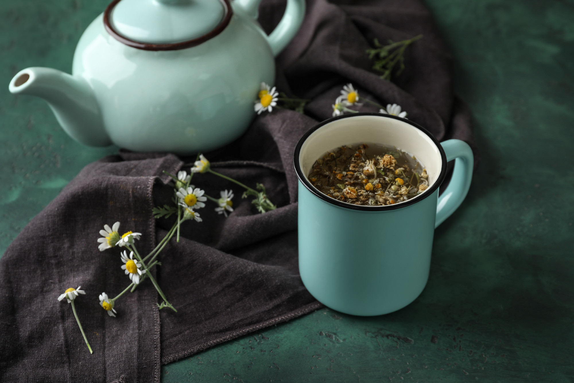 Cup and teapot with delicious camomile drink on green table�