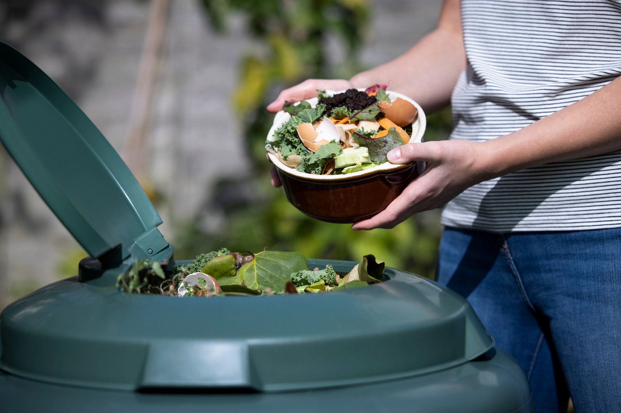 Close Up Of Woman Emptying Food Waste Into Garden Composter At H