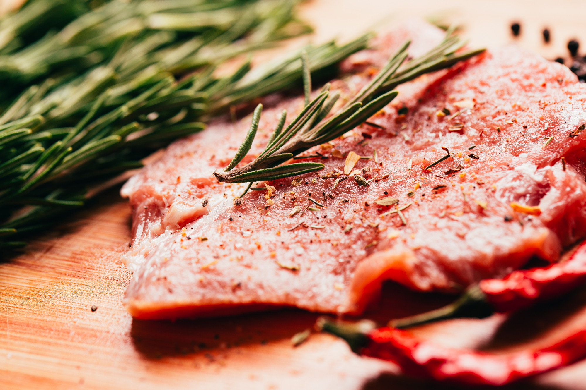 raw meat, sprig of rosemary and red hot pepper on a wooden light background