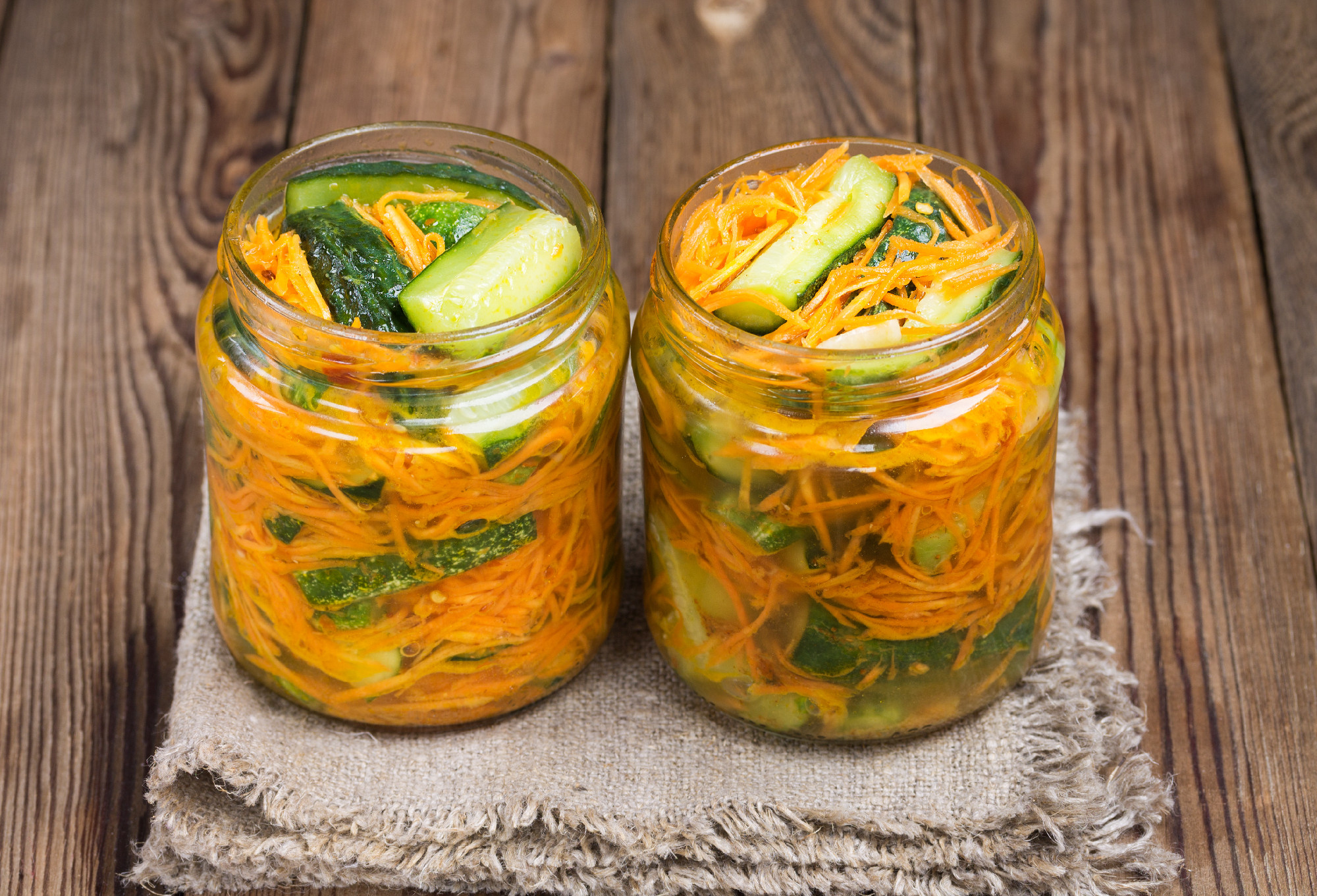 Traditional Korean snack of kimchi cucumbers in two glass jars: cucumbers marinated with carrots, hot pepper and garlic, with vegetable oil, on a napkin.