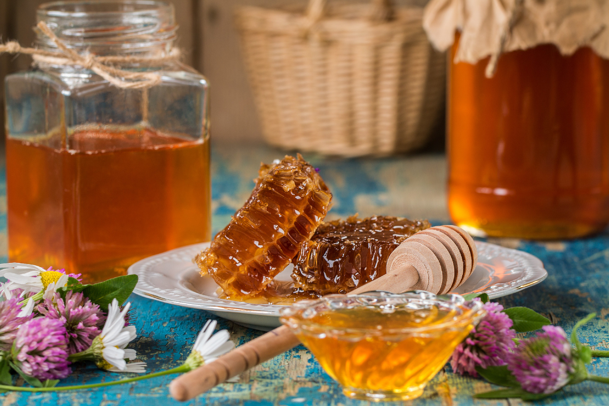 Two honey pots with honeycomb on a wooden table with flowers