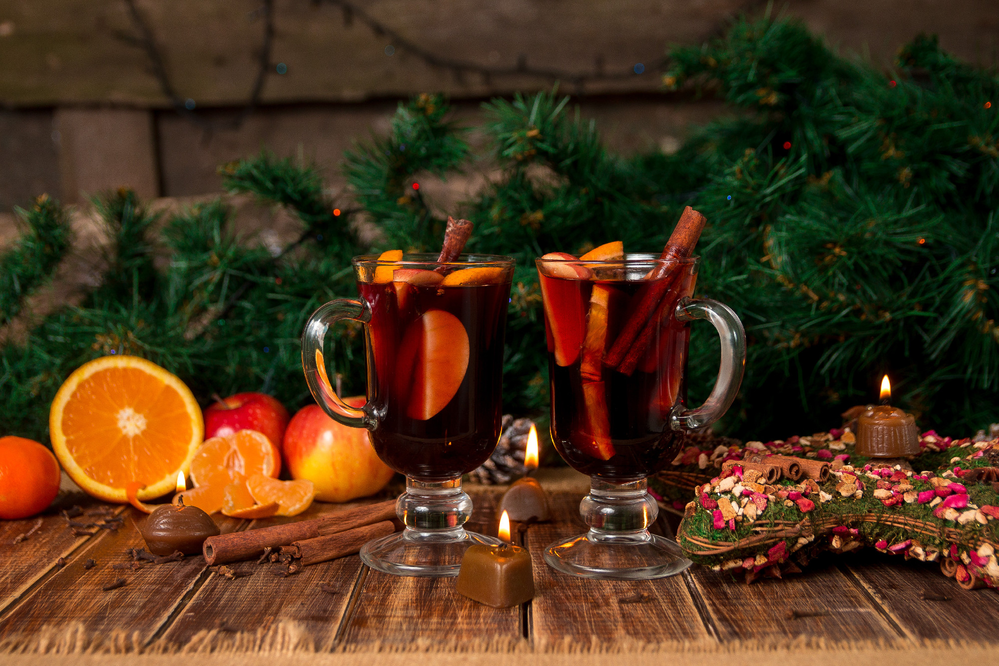 Christmas mulled wine with fruits and spices on wooden table. Xmas decorations in background. Two glasses. Winter warming drink recipe ingredients around.