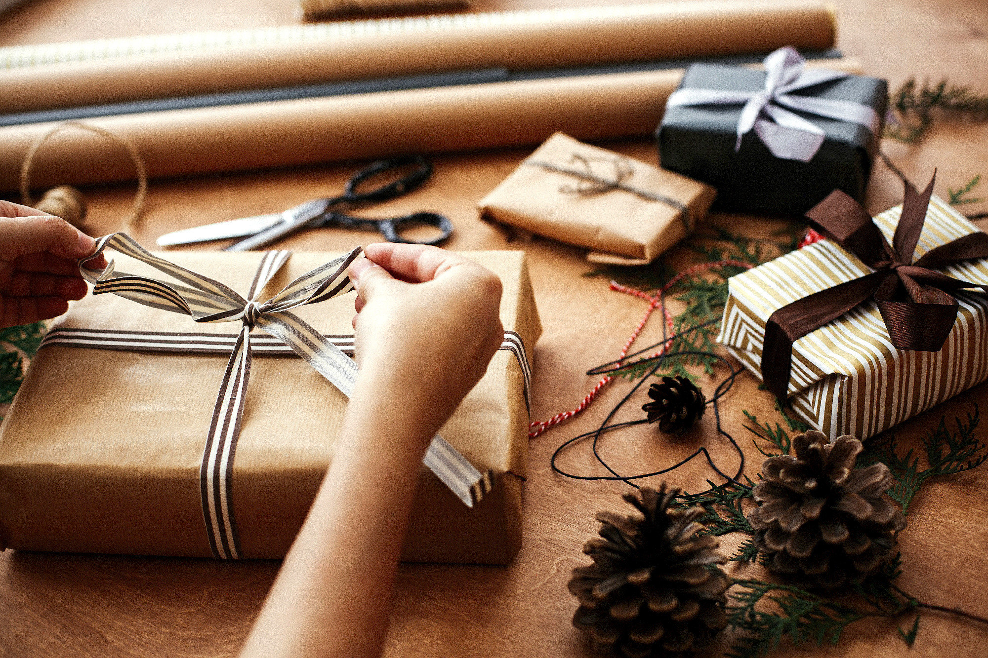 Hands wrapping stylish christmas gift box in craft paper and sci