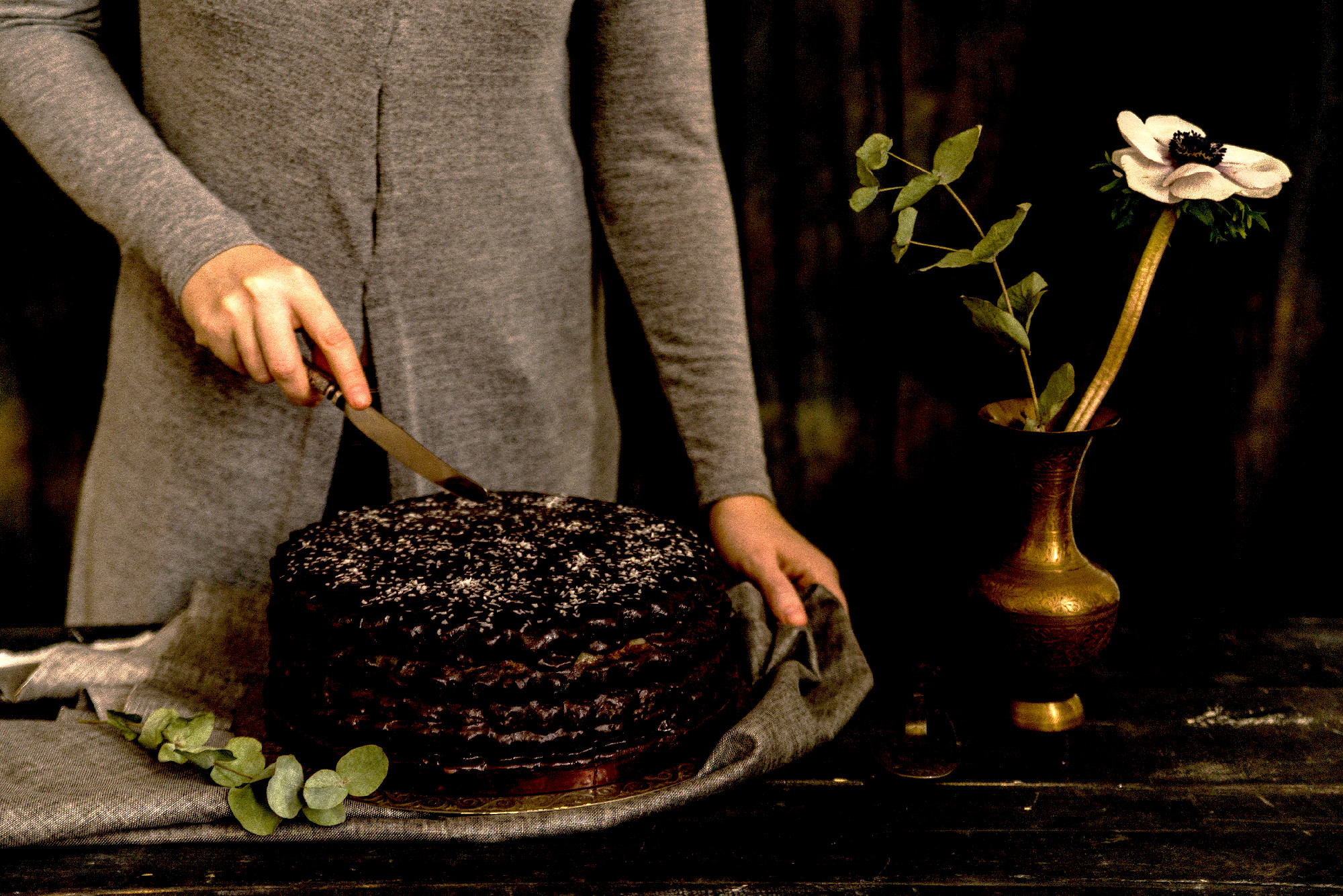 Woman cuts chocolate cake close. Dark tones
