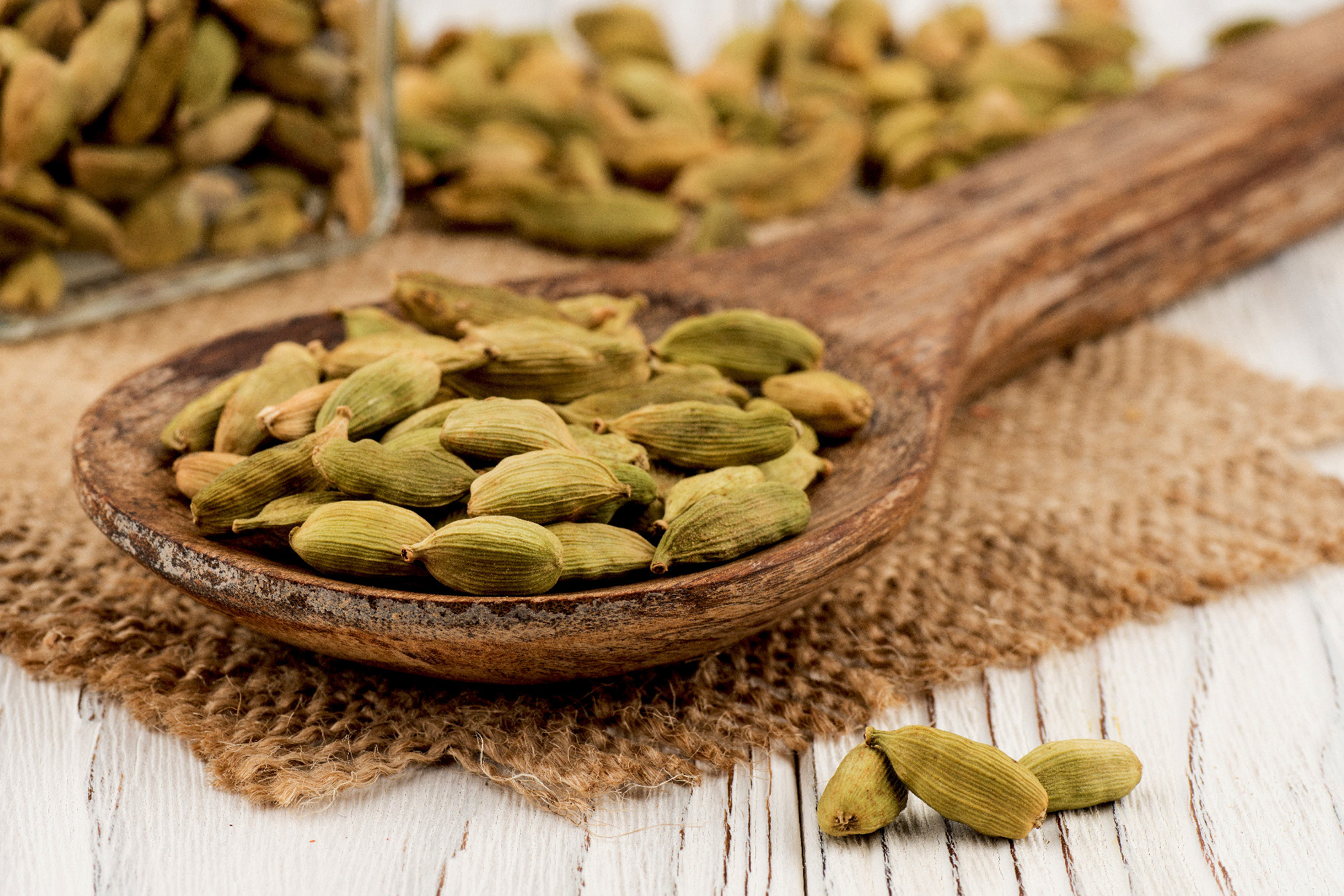 Cardamom in a wooden spoon and an old white wooden table.