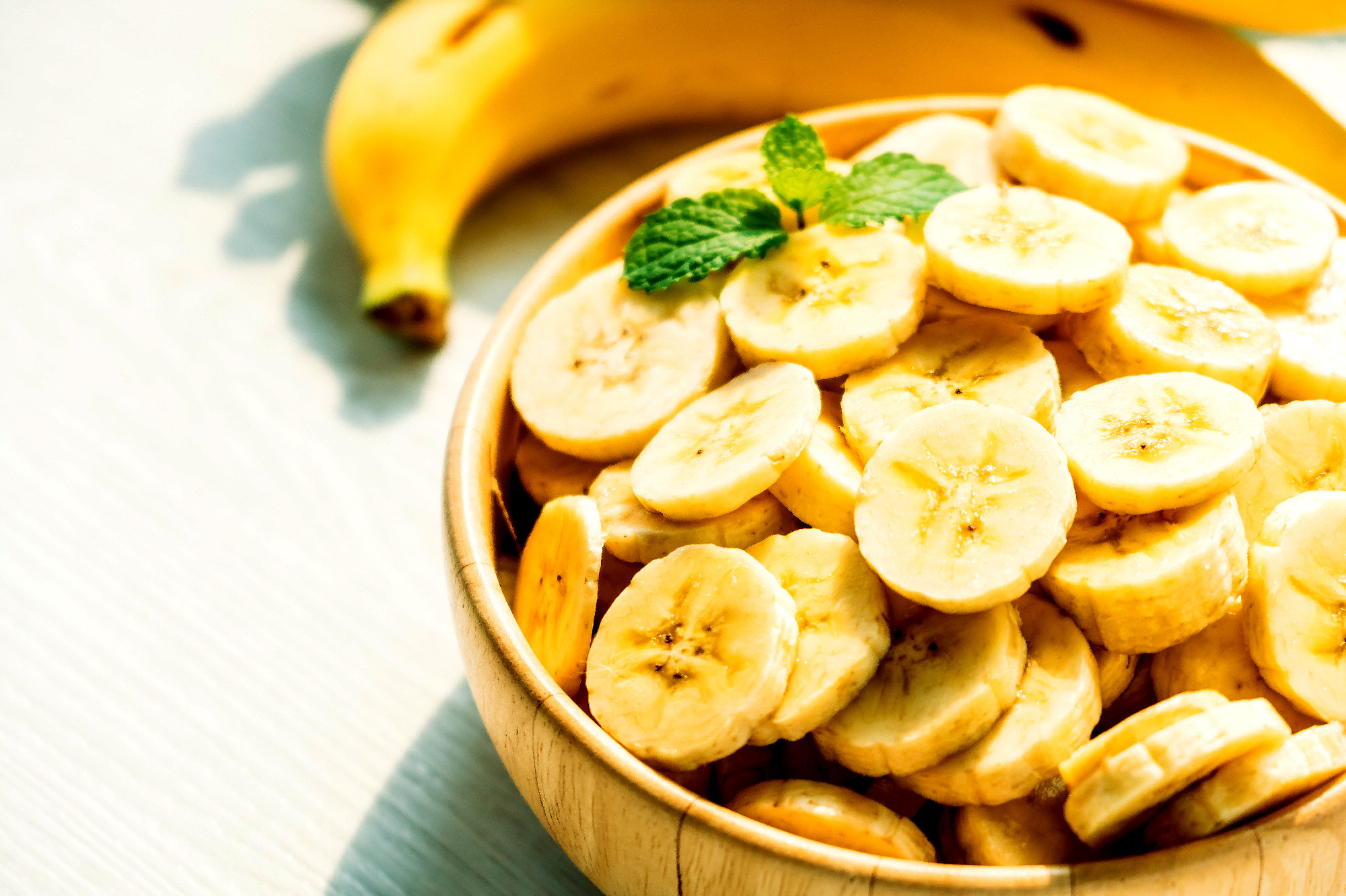 Raw yellow banana slices in wooden bowl