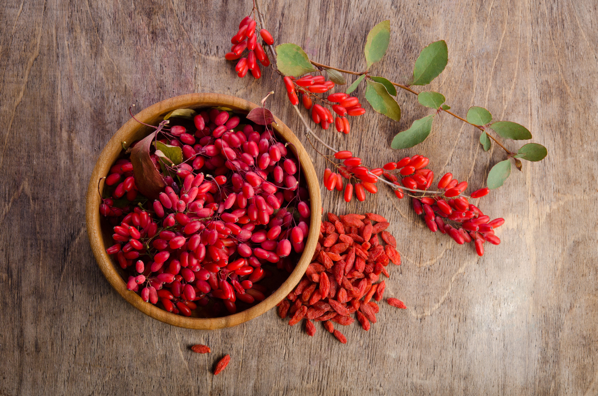 Barberry with leaves and dry goji berries on wooden background