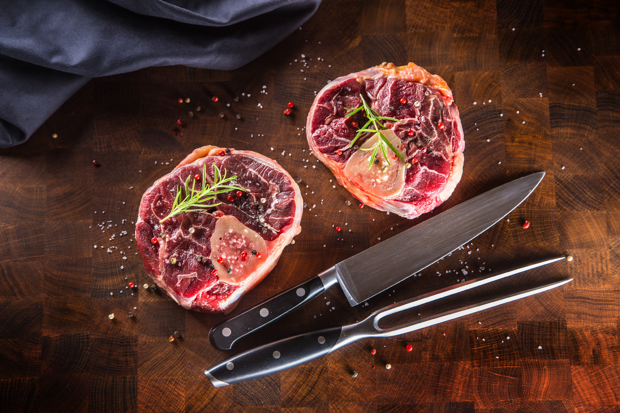 Two raw pieces beef shank on wooden butcher board with fork and