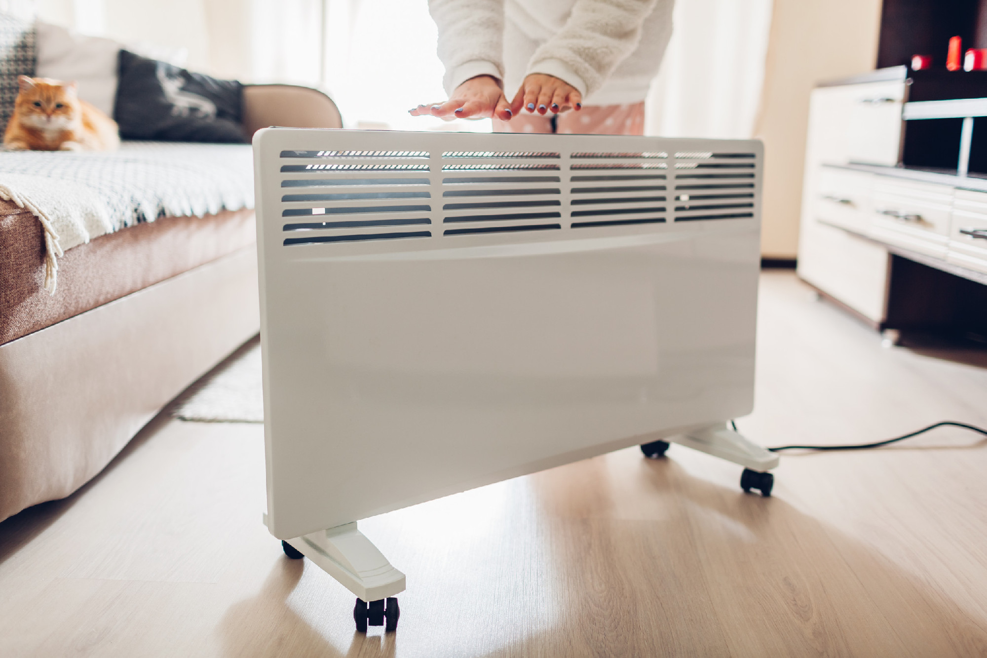Using heater at home in winter. Woman warming her hands. Heating season.