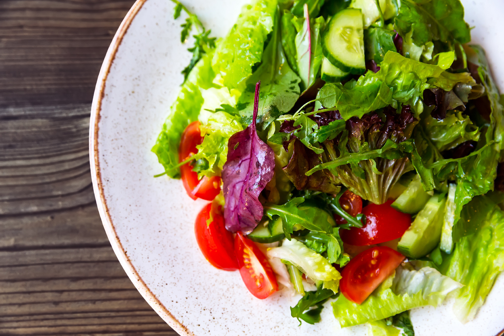 Bowl of salad with vegetables on wooden table.
