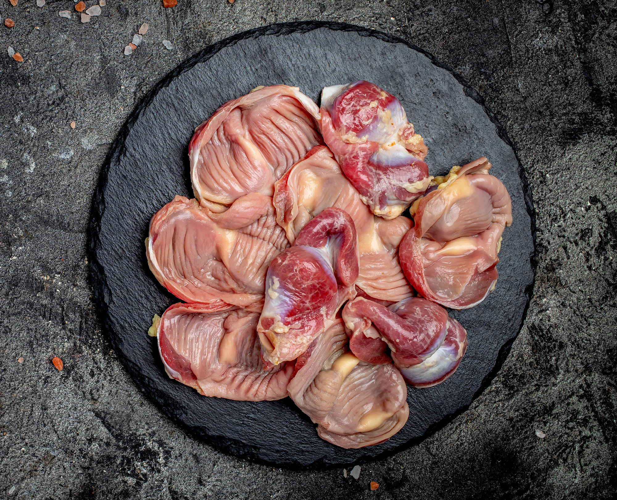 Raw uncooked chicken gizzards, stomach on a slate board. Traditi