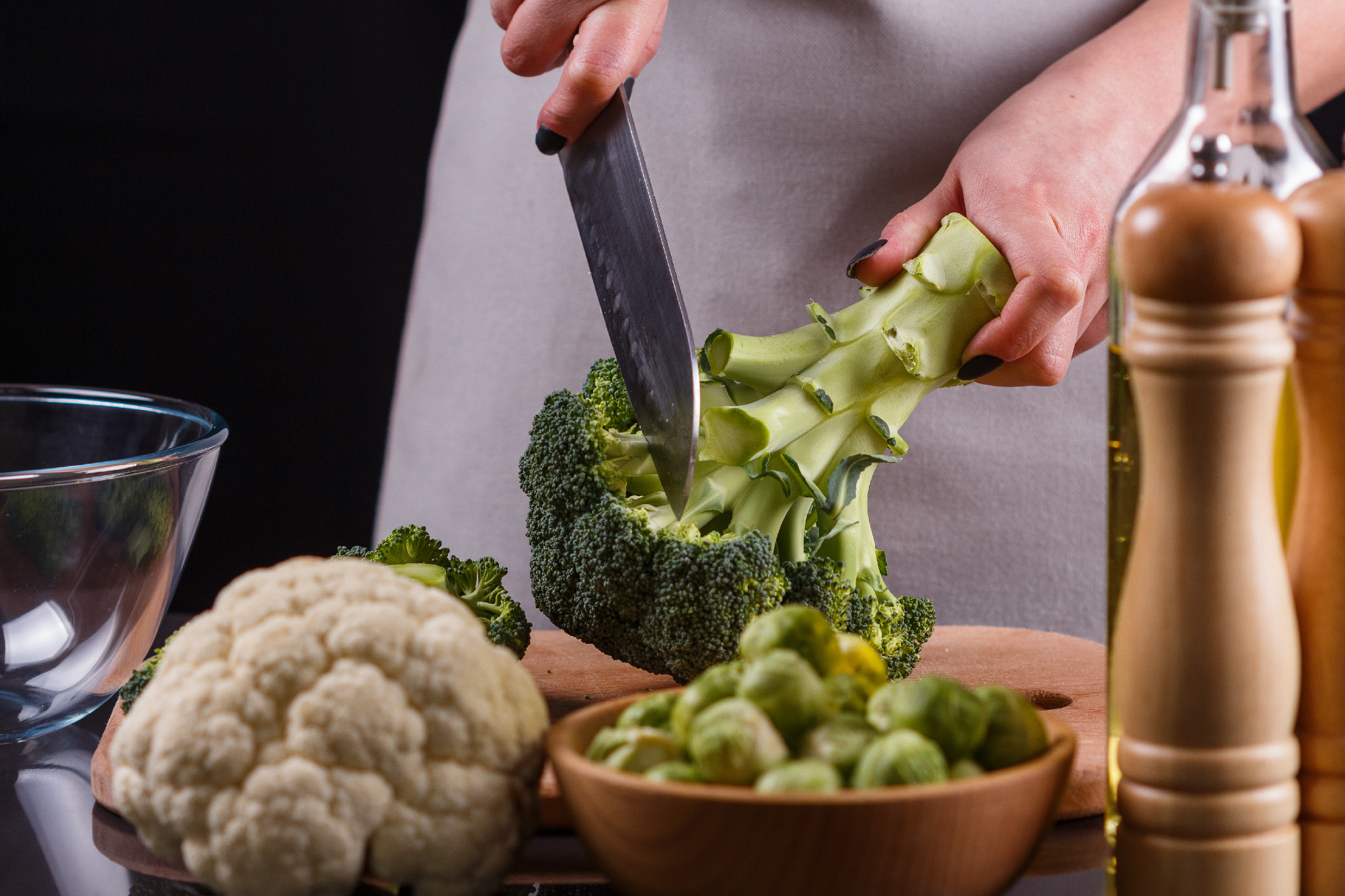 young woman in a gray aprons cuts cauliflower broccoli