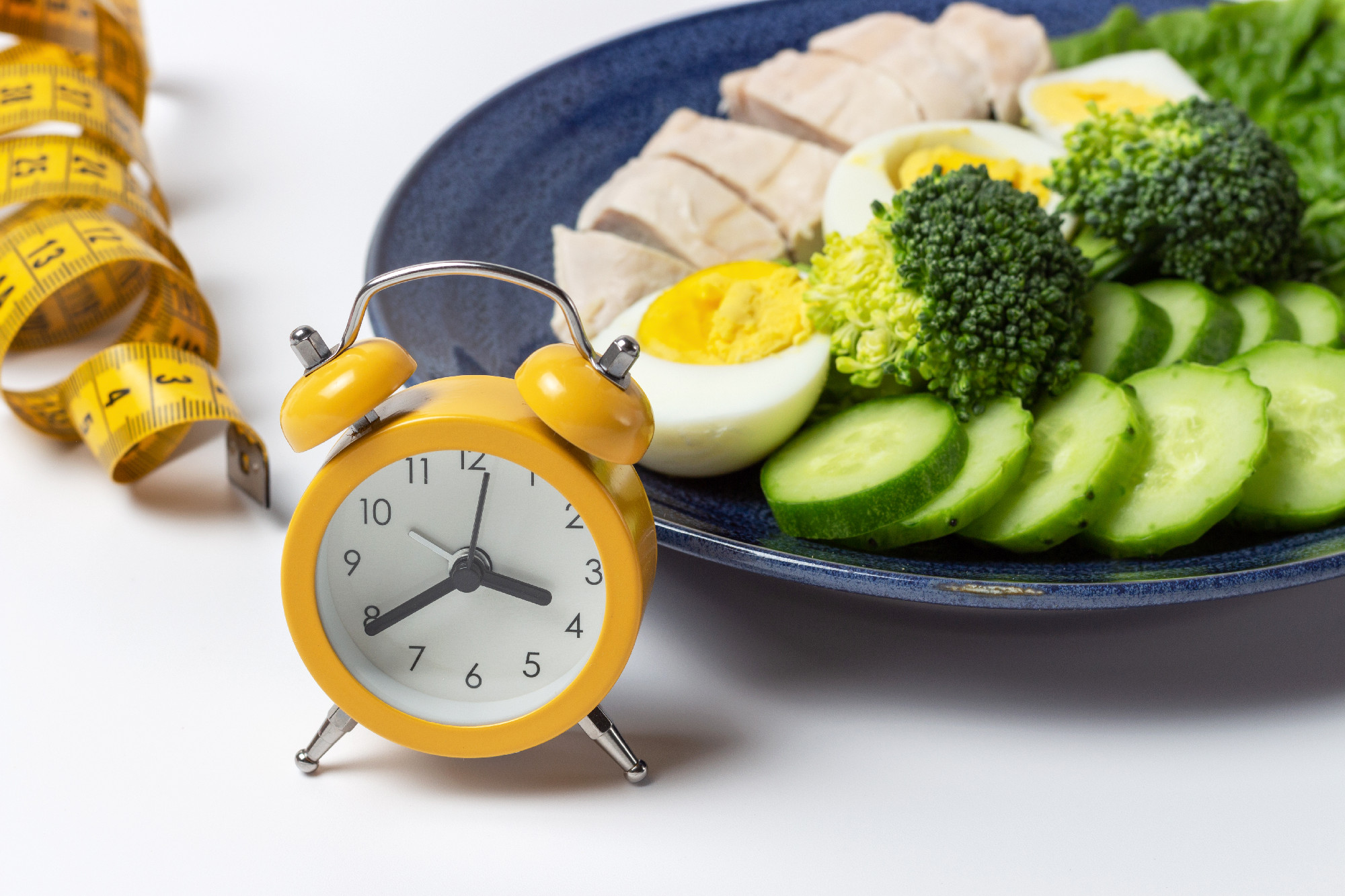 Plate with salad, alarm clock and measuring tape on white background