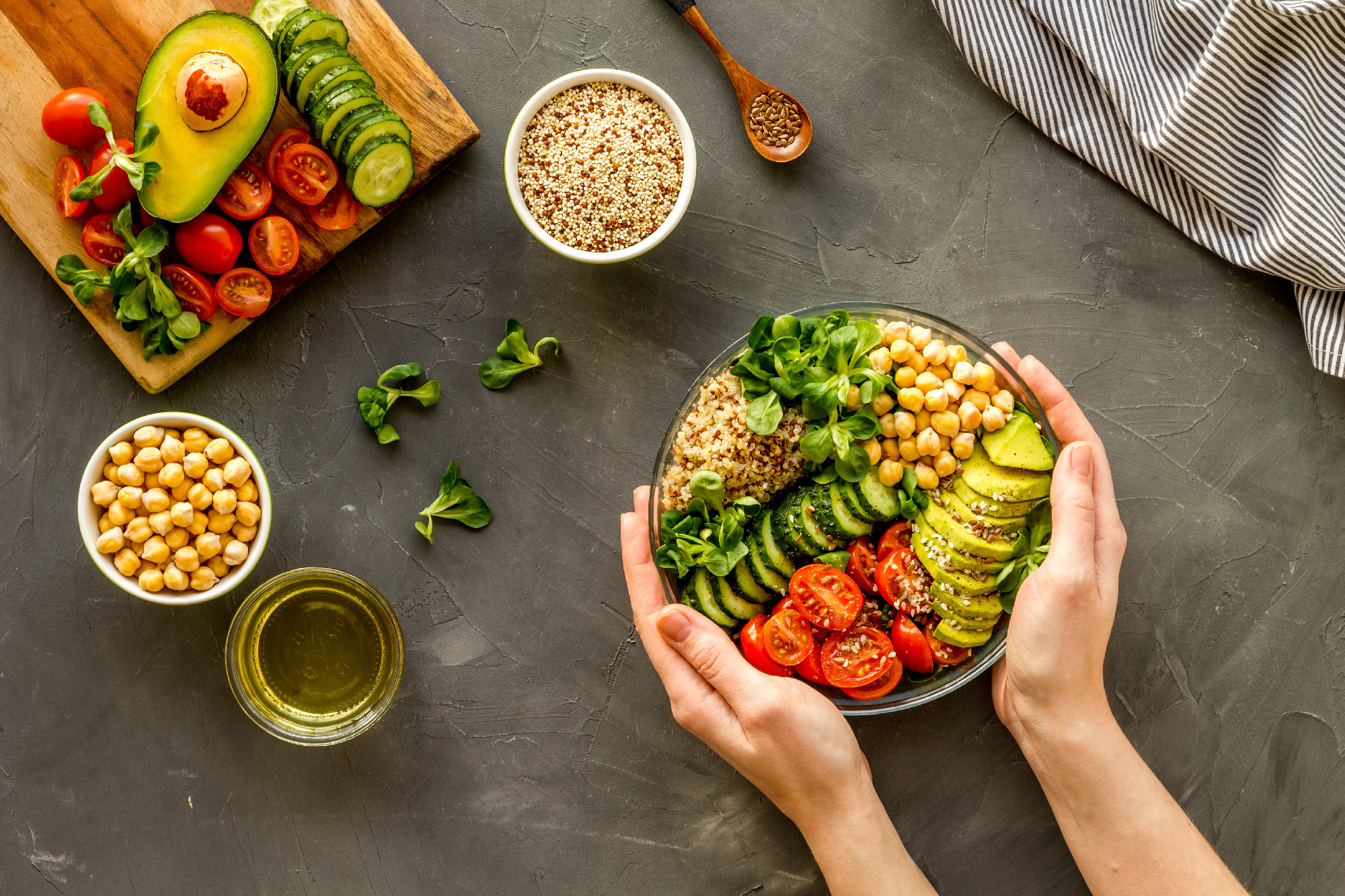 Quinoa, avocado and chickpeas in bowl in hands - balanced healthy food - on grey table. Top view