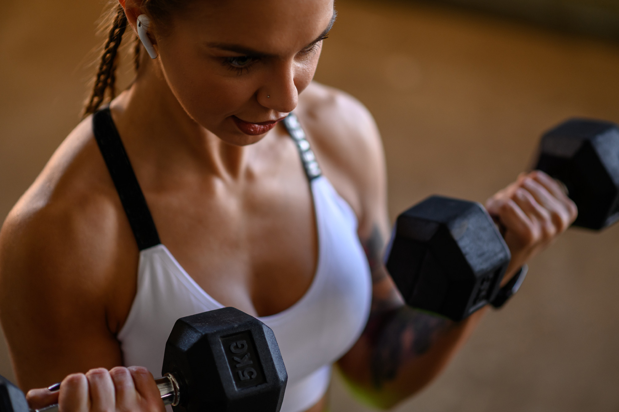 Woman training outside while using dumbbells and airpods