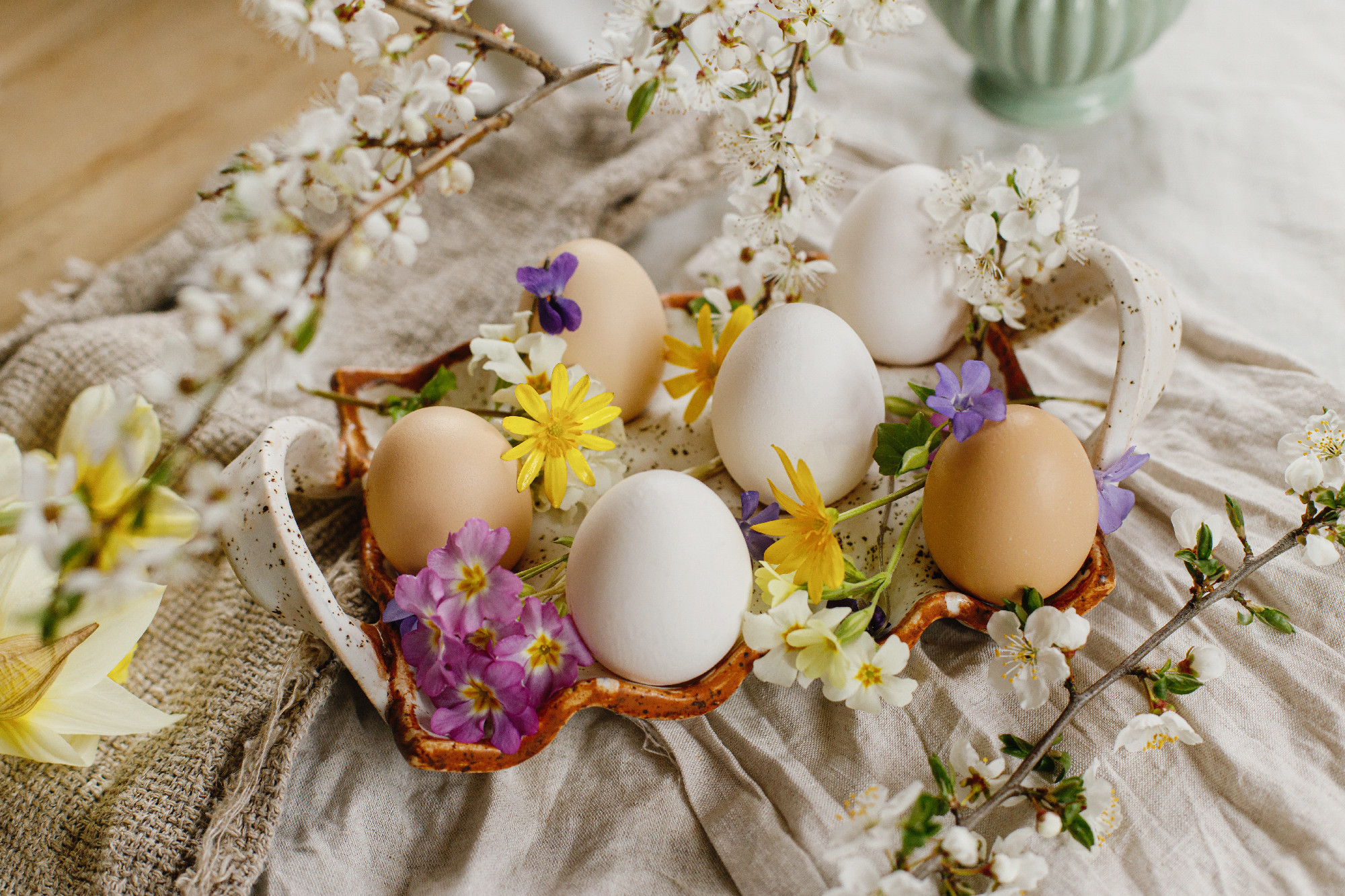 Stylish easter eggs and blooming spring flowers on linen fabric