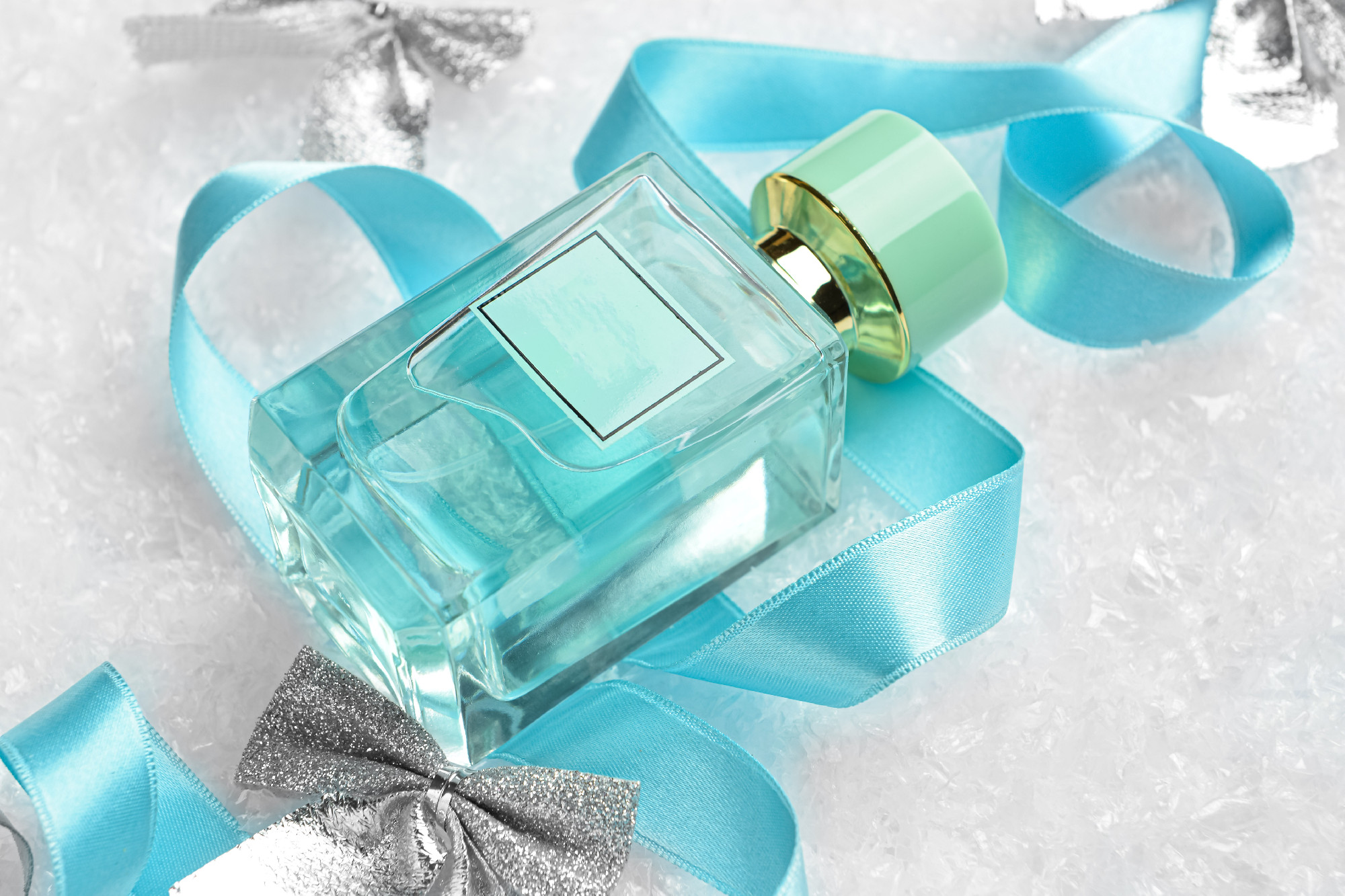Composition with bottle of perfume, ribbon and Christmas bows on snow background, closeup�