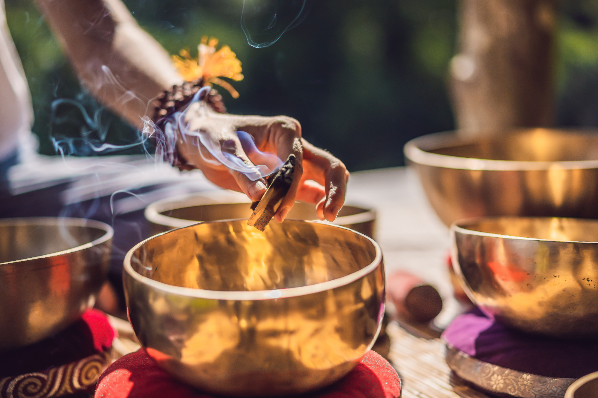 Woman playing on Tibetan singing bowl while sitting on yoga mat against a waterfall. Vintage tonned. Beautiful girl with mala beads meditating