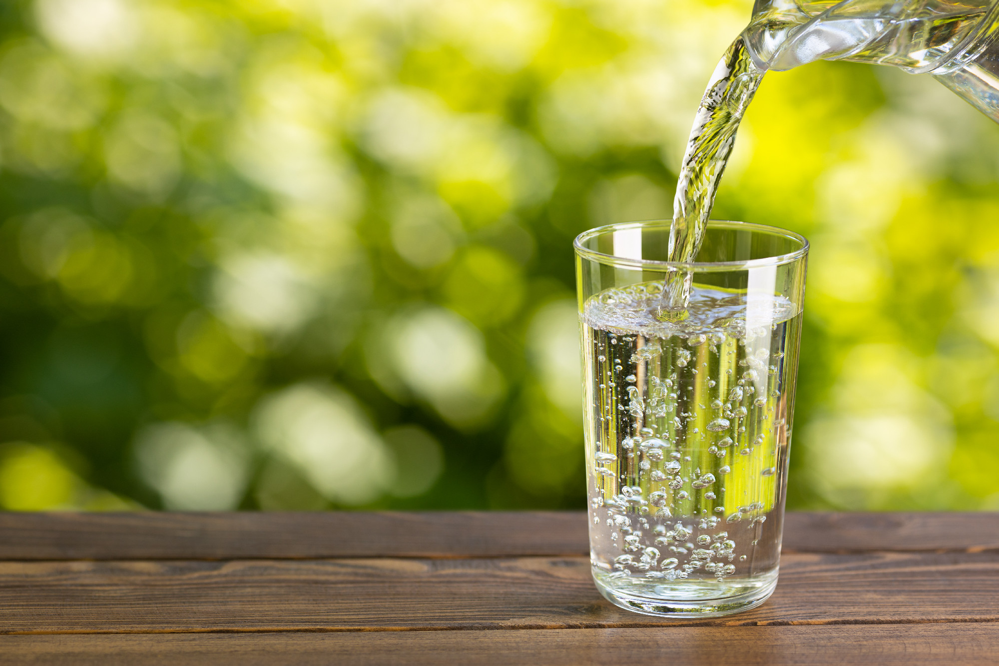 water from jug pouring into glass on table outdoors