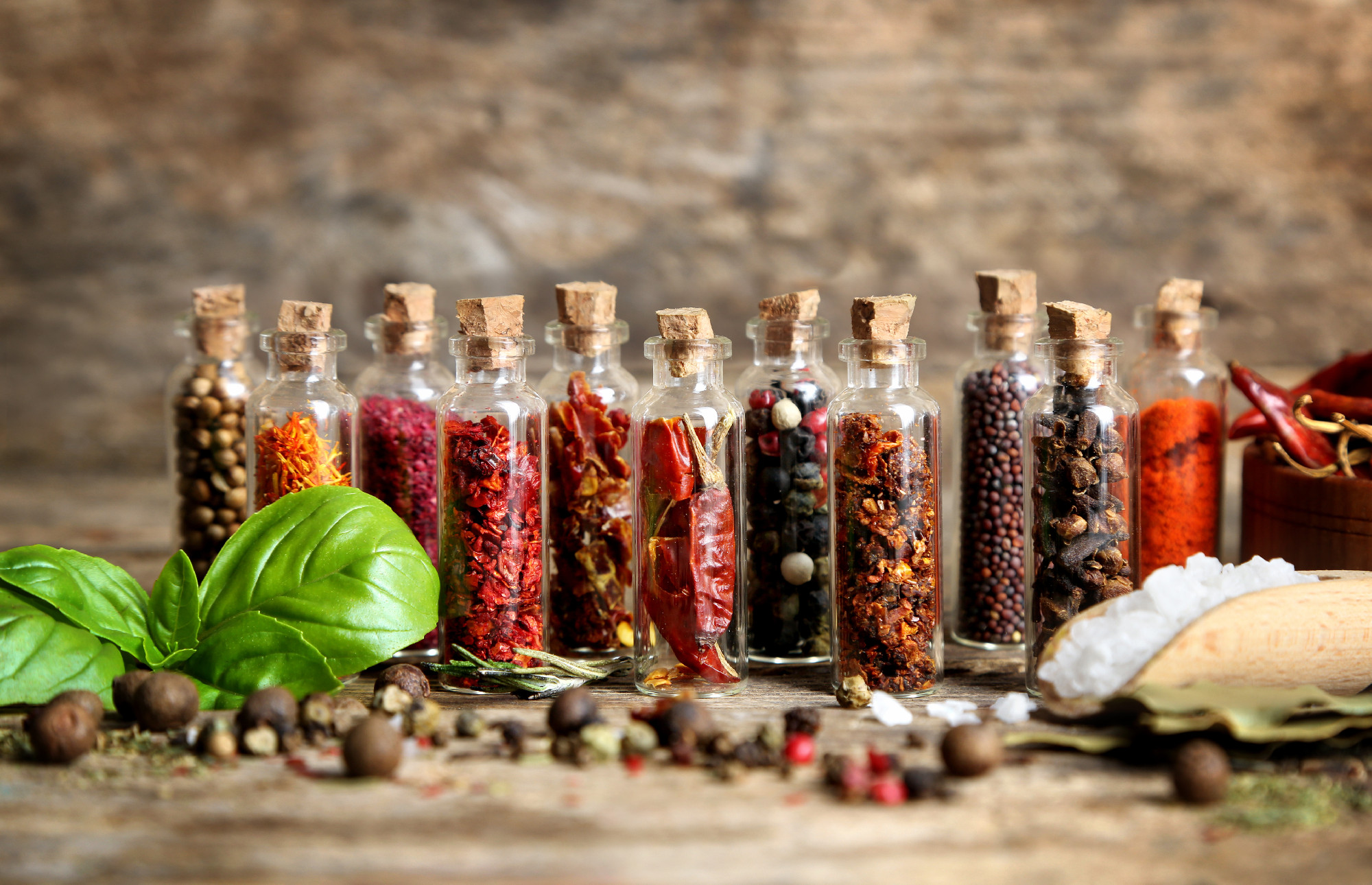 Assorted dry spices in glass bottles on wooden background