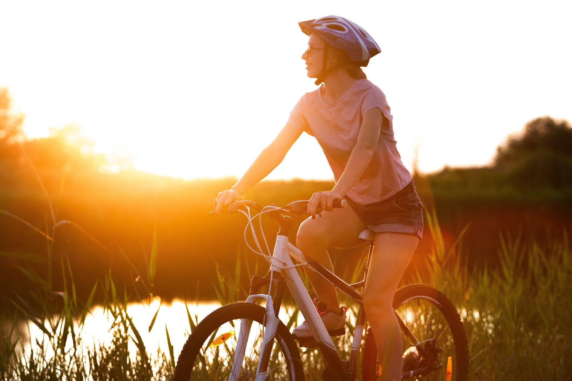 Joyful young woman riding a bicycle at the riverside and meadow promenade
