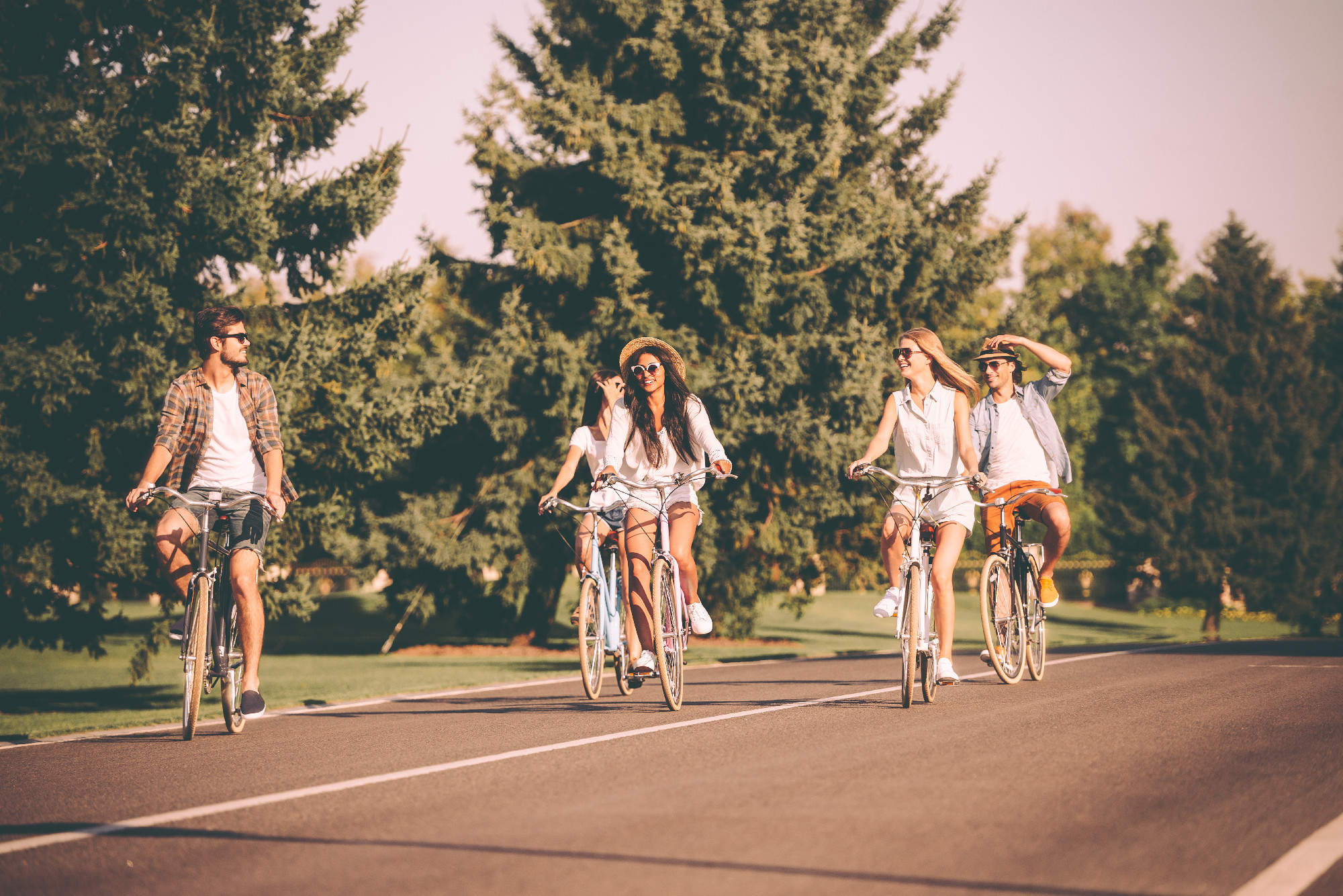 Great day for cycling. Group of young people riding bicycles along a road and looking happy