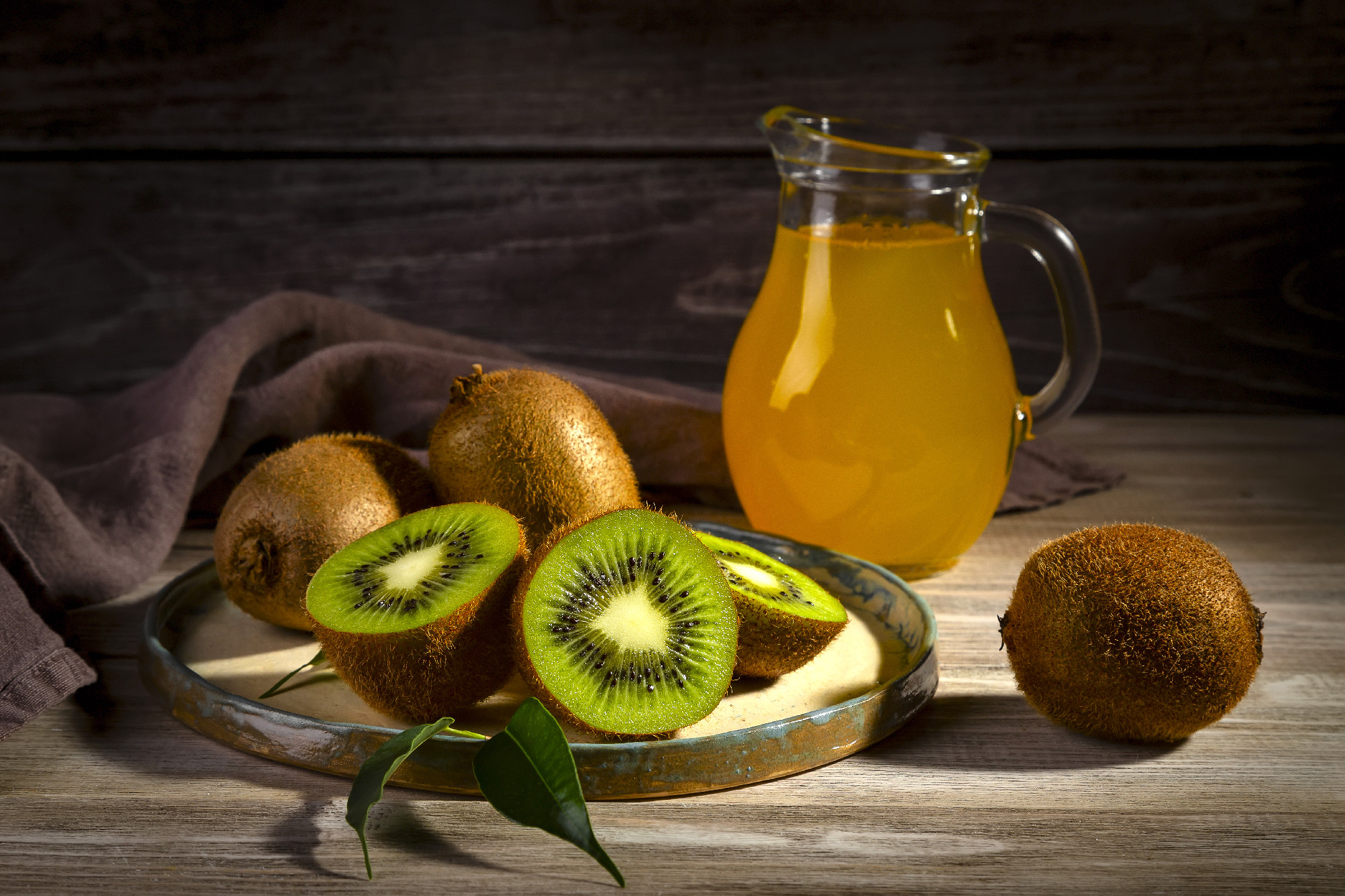 Kiwi in a plate on a wooden table and juice in a glass jug