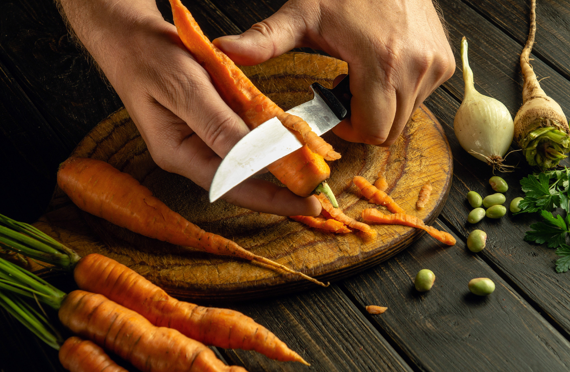 The cook hands with a knife peel the carrots on kitchen cutting