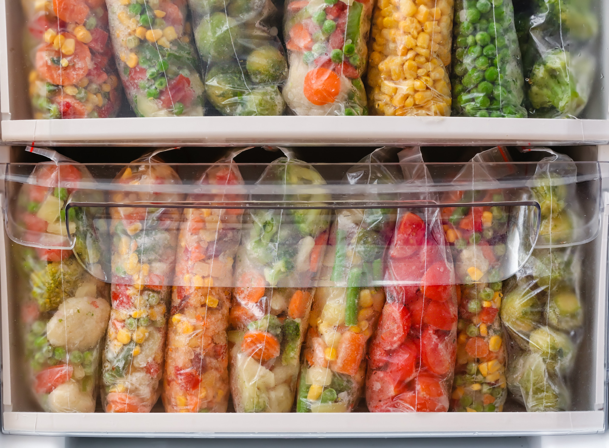 Plastic bags with frozen vegetables in refrigerator, closeup�