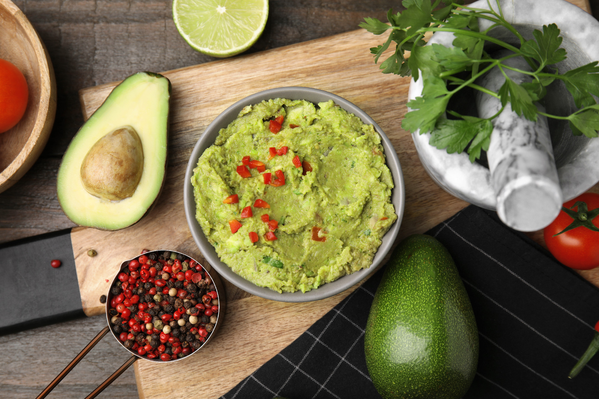 Bowl of delicious guacamole and ingredients on wooden table, fla