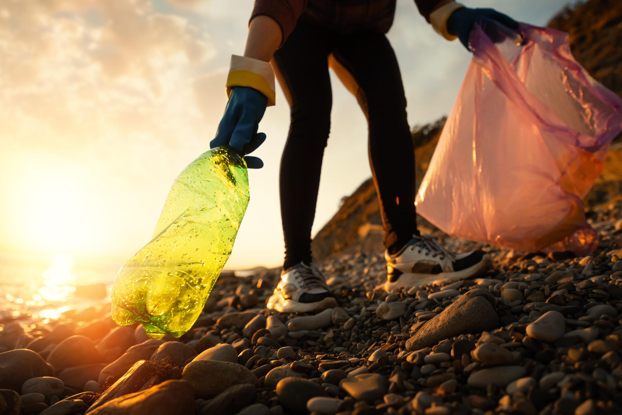 Conservation of ecology and Earth Day. A volunteer collects plastic bottles by the sea or river. Coastal cleanup for recycling. World environment day and pollution of seas and rivers concept